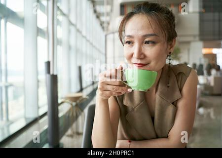 Reife asiatische Frau trinkt Tee im modernen Hotelrestaurant Stockfoto