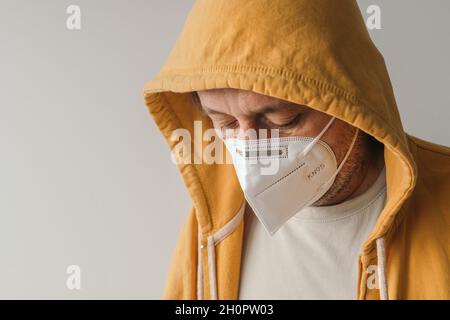 Lässiger Mann mit gelber Kapuzenjacke, der eine schützende Atemschutzmaske KN95 während der Covid-19-Pandemien trägt, selektiver Fokus Stockfoto