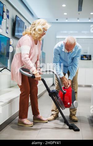 Glückliches Ehepaar, das einen neuen Staubsauger ausprobiert hat. Inneneinrichtung des Technikladens. Stockfoto