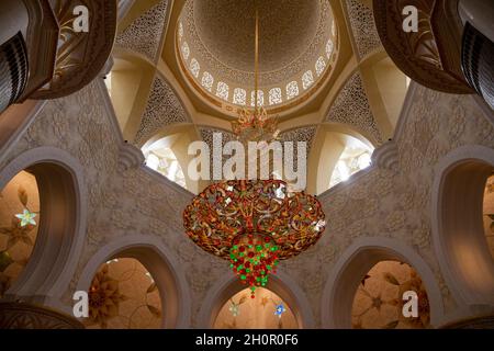 Abu Dhabi, Vereinigte Arabische Emirate. Elegante, moderne Lampe, die im Innenhof aufgehängt wird und Blick auf die große Moschee des Scheich Zayed (Masjid), Minarett des l Stockfoto