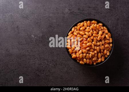 Weiße Bohnen in Tomatensauce in einer Schüssel auf schwarzem Schieferhintergrund Stockfoto