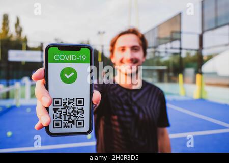 Junger Mann zeigt Impfpass covid-19 mit App auf Smartphone erster Sport, Coronavirus-Konzept Stockfoto