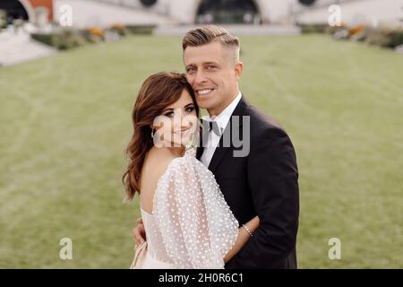 Porträt von Brautpaar von Braut und Bräutigam im Hochzeitskleid auf dem Hintergrund von grünem Gras lächelnd, glücklich Blick auf die Kamera. Stockfoto