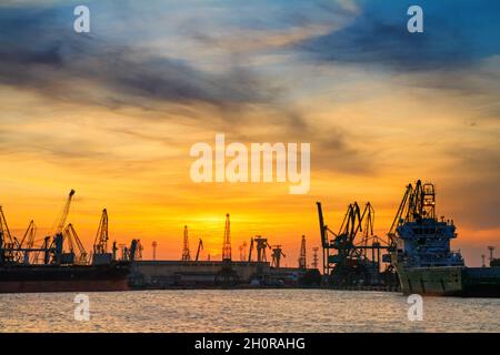 Silhouetten von Hafenkranen und Frachtschiffen im Seehafen vor dem Hintergrund des Sonnenuntergangs in Varna an der bulgarischen Schwarzmeerküste Stockfoto
