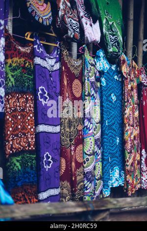 Eine Auswahl an farbenfrohen, bequemen, handgefärbten Batik-Kleidern aus Baumwolle und Seide hängt auf dem Display. Selektiver Fokus. Stockfoto