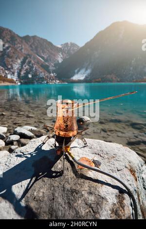 Kupfer Cezve mit Kaffee auf einem Gasherd im Herbst See Camping in den Bergen. Zubereitung von Kaffee im Freien Konzept Stockfoto