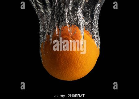 Frische, ganz orange Früchte im Wasser spritzen isoliert auf schwarzem Hintergrund. Minimales Lebensmittelkonzept. Stockfoto
