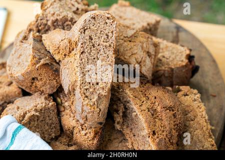 Frisch gebackenes braunes Brot, Maslin-Brot in einem kleinen Haufen auf einem braunen Holzteller, im Freien. Nahaufnahme mit der Textur des Brotes. Stockfoto