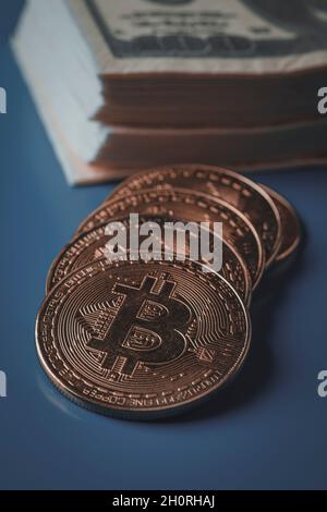 Nahaufnahme einiger Bitcoins und eines Stapels Dollarnoten auf blauem Hintergrund Stockfoto