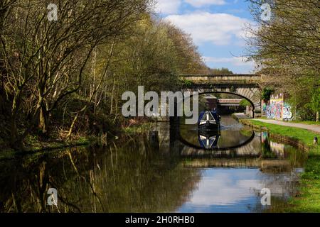 Narrowboat Segeln, Reisen auf sonnigen städtischen Binnenwasserstraßen (Mann & Hund an Bord, sonnenbeschienenen Schlepptau) - Leeds Liverpool Canal, Yorkshire, England, Großbritannien. Stockfoto