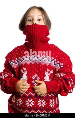 Schelmische Gesicht des kleinen Mädchens halb aus gestricktem Kragen aus Weihnachtspullover mit Rentieren, isoliert auf weißem Hintergrund Stockfoto