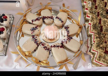 Designer-Kuchen in Eisglasur, auf Stöcken, auf Teller, auf weißer Tischdecke zwischen Tisch, Sweet Food Concept Small Business oder Konditorei Stockfoto