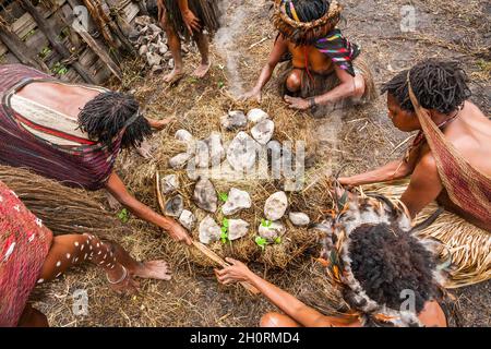 Wamena, Indonesien - 9. Januar 2010: Dani Frauen kochen Essen in einem Loch mit heißen Steinen gefüllt Stockfoto