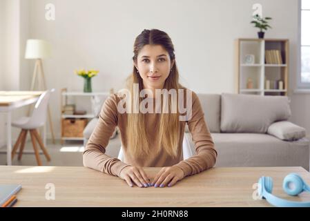 Porträt einer netten, freundlichen jungen Frau, die Webcam anschaut, während sie zu Hause im Wohnzimmer sitzt. Stockfoto