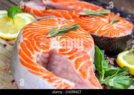 Draufsicht auf rohe Fischscheiben aus rotem Lachs mit Kräutern, Gewürzen und Zitrone in der Küche auf hellem Holzhintergrund, bereit zum Kochen aus nächster Nähe. Stockfoto