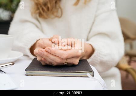 Nahaufnahme der Hände einer Frau, die auf einem Notizbuch zusammengeklemmt sind und an einem Kaffeetisch in Weißrussland sitzen Stockfoto