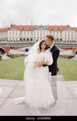 Foto von Braut und Bräutigam im Hochzeitskleid, umarmt vor dem Hintergrund der europäischen Altstadt, lächelnd und mit Blick auf die Kamera. Hochzeitstag. Hap Stockfoto