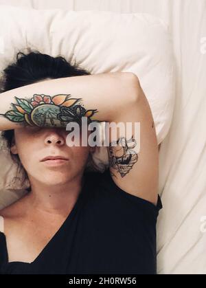 Ansicht von oben einer Frau, die mit ihrem Arm über ihrem Gesicht im Bett liegt Stockfoto