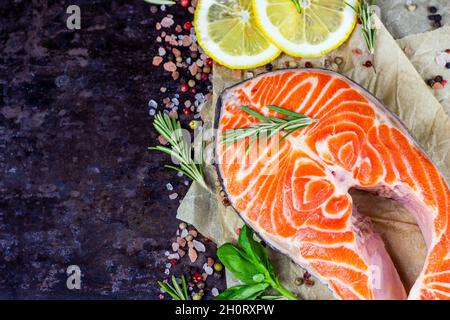 Rohe Fischscheiben mit rotem Lachs mit Kräutern, Gewürzen und Zitrone in der Küche auf dunklem Hintergrund mit Kopierplatz zum Kochen bereit. Stockfoto