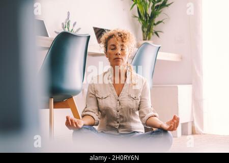 Frau machen loto-Position zu Hause, um sich zu entspannen und sich zu wohlfühlen. Drinnen gibt es entspannte Aktivitäten für Erwachsene Frauen, die auf dem Boden sitzen. Wohnzimmer Haus Innenausstattung Stockfoto