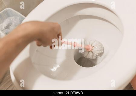 Die Hand des Typen hält die Toilettenbürste und reinigt die Toilette. Das Konzept der häuslichen Reinigung und Hygiene im Badezimmer. Stockfoto