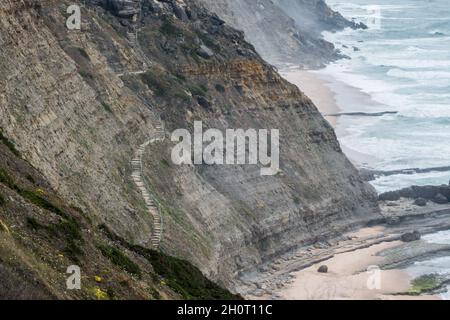 Ein abgeschiedener Strand, der über eine Treppe in eine steile Felswand in sedimentär erodierten Felsen an der Atlantikküste von Sintra in Portugal gelangt Stockfoto