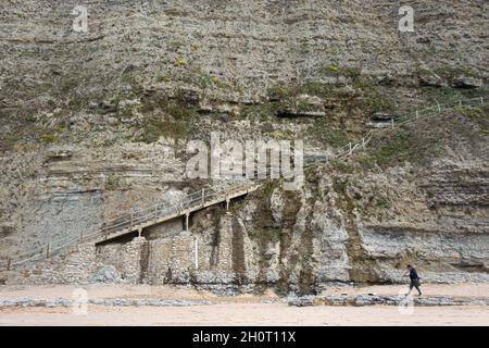 Sintra, Portugal - 24. Juni 2020: Ein Fischer mit Rute auf der Schulter verlässt den Strand über eine Treppe, die in eine vertikale Felswand in Küstenklippen eingebettet ist Stockfoto