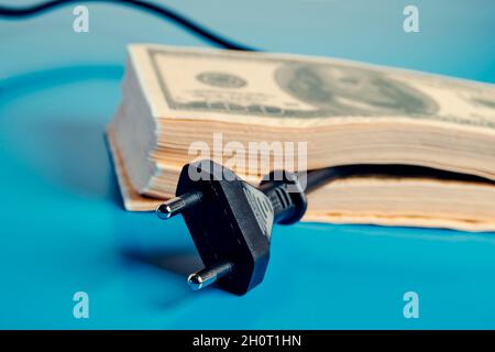 Ein Elektrokabel, das aus einem Stapel von Dollar-Banknoten entsteht und den hohen Strompreis darstellt Stockfoto