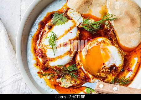 Türkische Eier cilbir in einer weißen Schüssel. Konzept der türkischen Küche. Pochierte Eier mit Joghurt und würziger Buttersauce, Nahaufnahme. Stockfoto