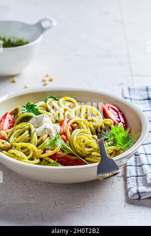 Spaghetti mit Pesto-Sauce, Oliven, Tomaten und Pinienkernen in einer weißen Schüssel. Italienisches Küchenkonzept. Stockfoto