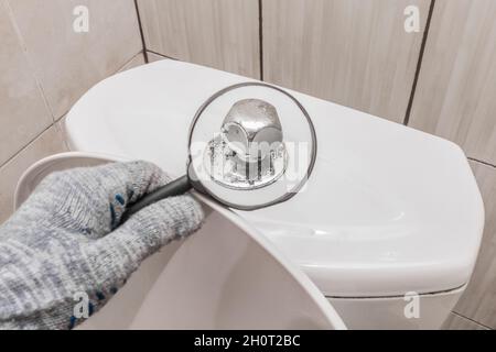 Die Hand eines Klempners in einem Bauhandschuh überprüft die Gebrauchstauglichkeit des Toilettenfasses. Professionelle Reparatur von sanitären Räumen. Stockfoto