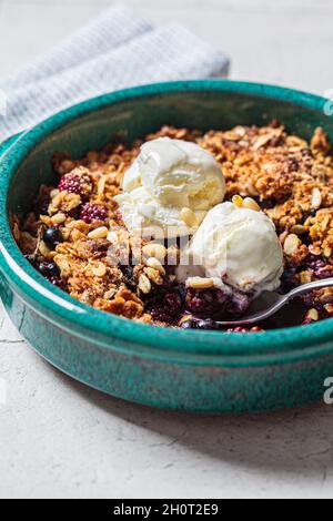 Beerenkrümelkuchen mit Eis in blauer Backform, Hintergrund mit grauen Fliesen, Nahaufnahme. Stockfoto