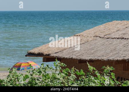 Ländliche Dach aus Rohr oder Schilf Stroh trocken auf dem Hintergrund der Küste, Strand und Wasser mit Horizont Linie. Stockfoto