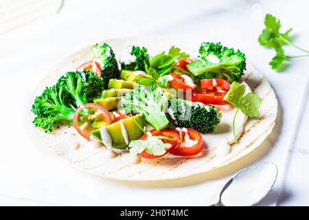 Vegane Tortilla mit Brokkoli, Avocado und Tahini-Dressing auf weißem Marmorboden. Vegetarisches Fast Food. Stockfoto