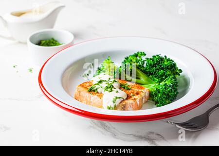 Gebratener Lachs mit cremiger Sauce und Brokkoli auf einem weißen Teller. Gesundes Lebensmittelkonzept. Stockfoto