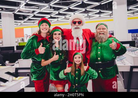 Portrait von attraktiven funky fröhlichen Unternehmen Elfen Auswahl Geschenke Advent Zeit zeigt Thumbup im Einkaufszentrum im Inneren Stockfoto