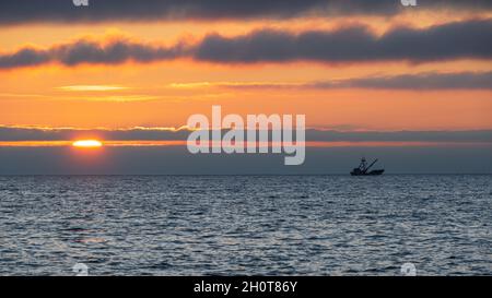 Ein Fischerboot in Silhouette, wenn die Sonne über dem Pazifik am Ende eines Sommertages vor dem Asilomar State Beach in der Nähe von Monterey California untergeht. Stockfoto