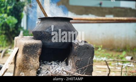 Wasser oder etwas, das auf einer Aluminiumpfanne gekocht wird, die auf einem irdenen Ofen mit Holz als Brennstoff in einem Dorf in Indien gehalten wird. Stockfoto