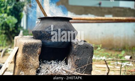 Wasser oder etwas, das auf einer Aluminiumpfanne gekocht wird, die auf einem irdenen Ofen mit Holz als Brennstoff in einem Dorf in Indien gehalten wird. Stockfoto
