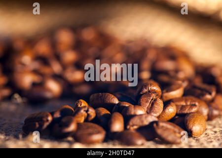 Nahaufnahme von frisch gerösteten Kaffeebohnen, die aus einem Sackleinen mit geringer Schärfentiefe gestreut wurden. Stockfoto