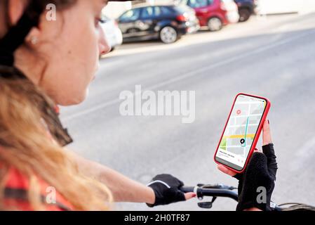 Eine Radfahrerin überprüft die Adresse ihrer nächsten Lieferung mit ihrem Mobiltelefon Stockfoto