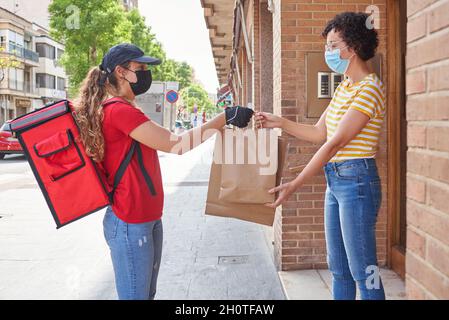 Ein Liefermädchen mit Gesichtsmaske liefert Beutel mit Lebensmitteln auf die Straße Stockfoto