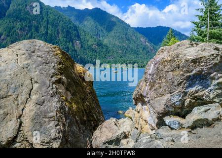 Einladender Blick auf das blaue Wasser und die Wälder des Lake Cushman durch die Felsbrocken am See Stockfoto