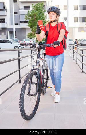 Eine Radfahrerin überprüft die Adresse ihrer nächsten Lieferung mit ihrem Mobiltelefon Stockfoto