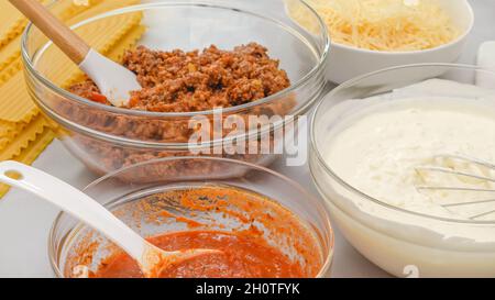Lasagne-Nudeln, Marinara, Hackfleisch, Frischkäse und Parmesankäse in Schüsseln. Zutaten für Rindfleisch Lasagne Rezept Nahaufnahme auf Küchentisch. Stockfoto