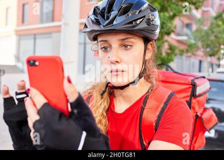 Eine Radfahrerin überprüft die Adresse ihrer nächsten Lieferung mit ihrem Mobiltelefon Stockfoto