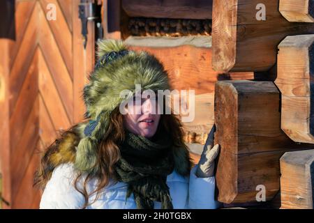 Glückliche Frauen, die im Schnee in der Nähe eines Holzhauses stehen und an einem frostigen Tag warm angezogen sind Stockfoto