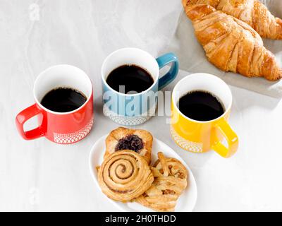 Drei Tassen schwarzen Kaffee, drei Gebäckstücke auf einem Teller und zwei Coissants Stockfoto