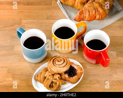 Drei Tassen schwarzen Kaffee, drei Gebäckstücke auf einem Teller und zwei Coissants Stockfoto