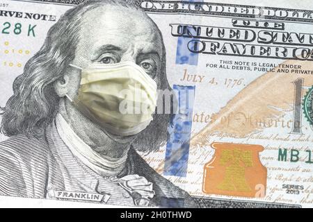 Nahaufnahme der US-amerikanischen Papierwährung einhundert-Dollar-Rechnung mit Benjamin Franklin trägt gelbe Arztmaske wegen COVID-19 Pandemie macht ein g Stockfoto